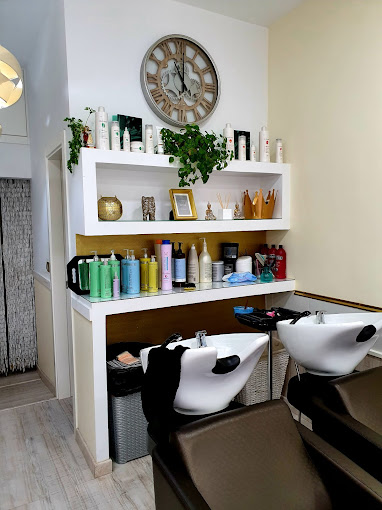 Estaciones de lavado de cabello en la peluquería "Laura García", con sillas negras y estanterías llenas de productos para el cabello, decoradas con un reloj y plantas.